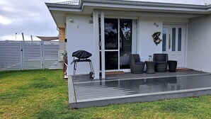Een modern huis met een overdekte veranda, een barbecue en tuinmeubilair.