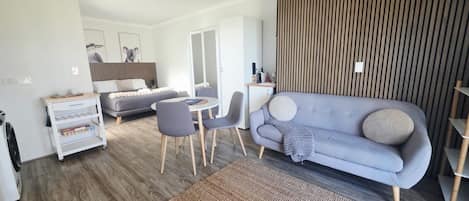 A modern living room with a grey sofa, a dining table, and a kitchen area.