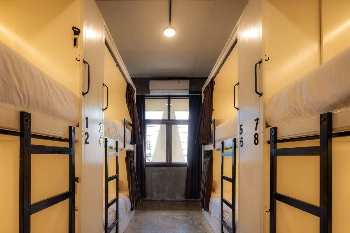 A corridor with bunk beds numbered 1 to 8, a ceiling light, and a window at the end.