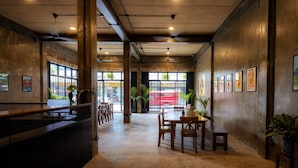 A spacious indoor area with a reception desk, wooden tables, chairs, and potted plants. - Lanna Loft Hostel (Chiang Mai)