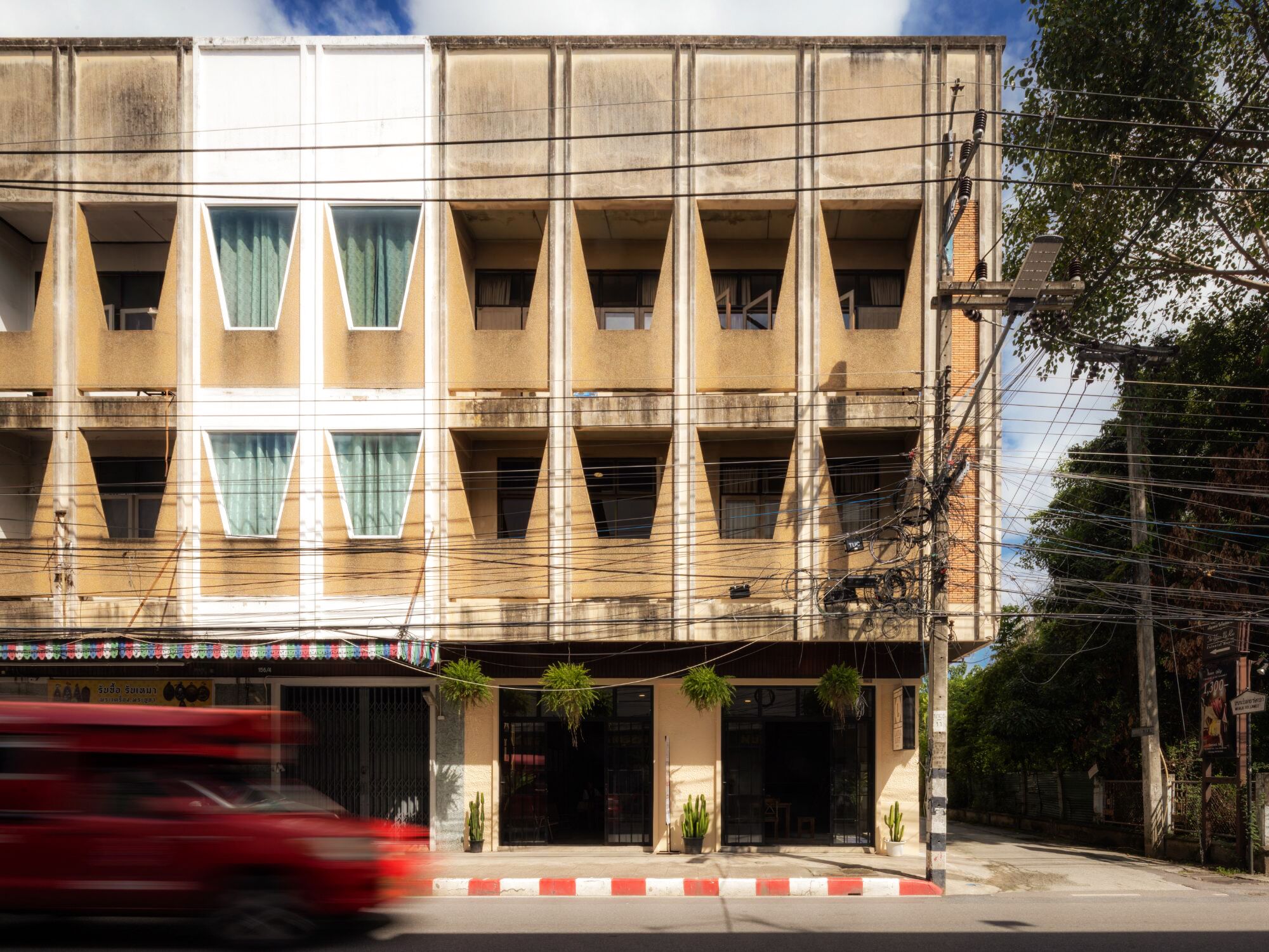 A multi-story building with a symmetrical facade, featuring triangular window patterns and a central entrance with potted plants.
