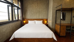 A hotel room with a large bed, wooden headboard, two bedside lamps, a desk with a chair, and a mirror. - Lanna Loft Hostel (Chiang Mai)