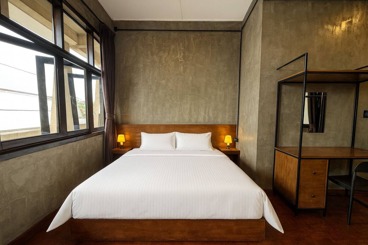 A hotel room with a large bed, wooden headboard, two bedside lamps, a desk with a chair, and a mirror.