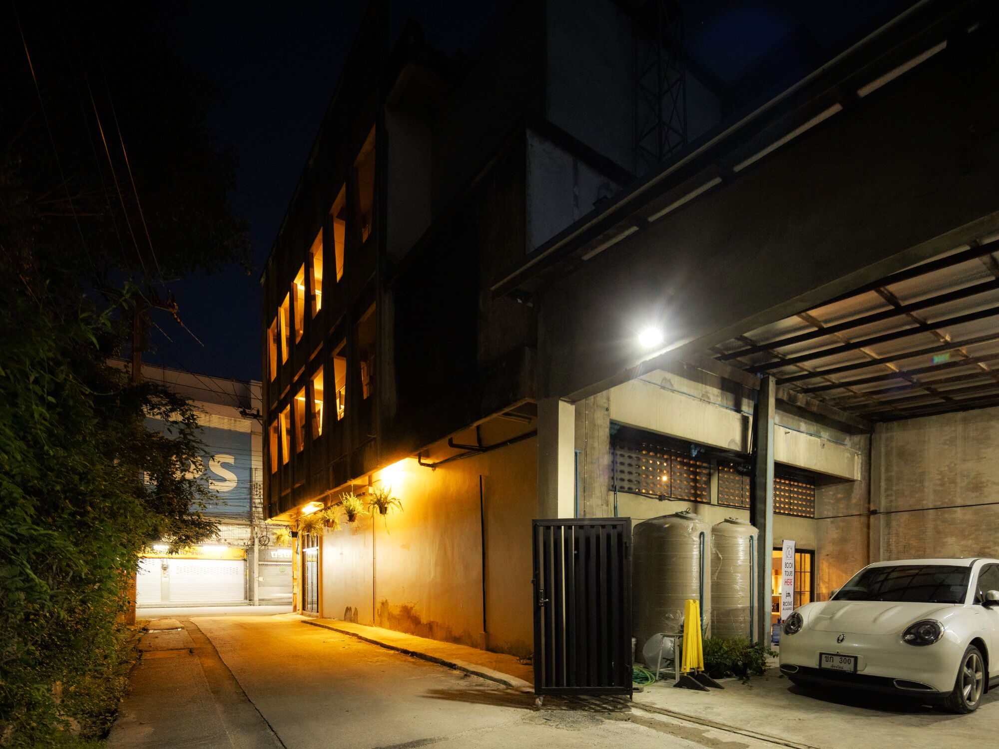 Una calle urbana iluminada de noche, con un coche blanco estacionado en un área de aparcamiento techada.