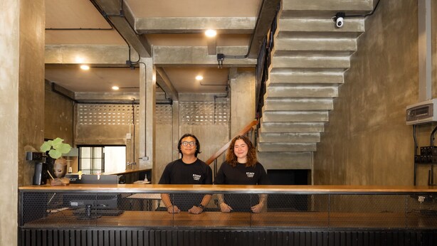 A reception area with a counter, two staff members, a coffee machine, and a staircase. - Lanna Loft Hostel (Chiang Mai)