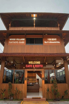 A two-story wooden building with a sign indicating 'Wood Village Gayang Sari' and 'For Rent Rp.11 J/month/Villa'. - Wood Village Nusa Dua Bali (Kutuh)
