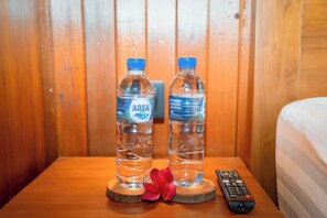 Two water bottles on a wooden nightstand with a remote control and a red flower.