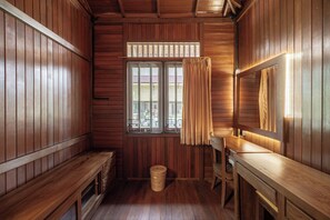 A wooden cabin room with a bench, a table, a window with curtains, and a mirror.
