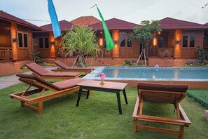 Uma área na piscina com espreguiçadeiras de madeira, uma mesa e uma piscina pequena.