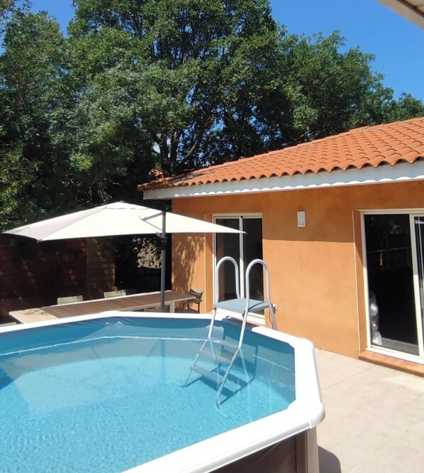 A swimming pool with a ladder, a covered seating area, and a building with a tiled roof.