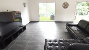 Sala de estar con televisor de pantalla plana, sofá de cuero y puerta corrediza de vidrio que da a un patio.