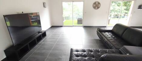 A living room with a flat-screen TV, a leather sofa, and a sliding glass door leading to a patio.