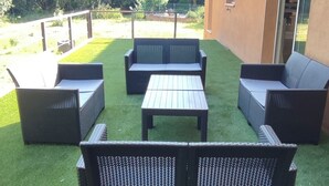 Un patio al aire libre con mobiliario de mimbre, una mesa y vistas a un paisaje verde y colinas al fondo.