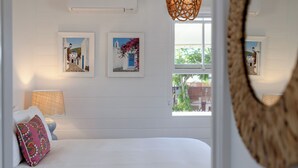 A bedroom with a large bed, two wall-mounted pictures, a window, and a hanging light fixture. - Sunset Cottage on the Burrum River (Burrum Heads)