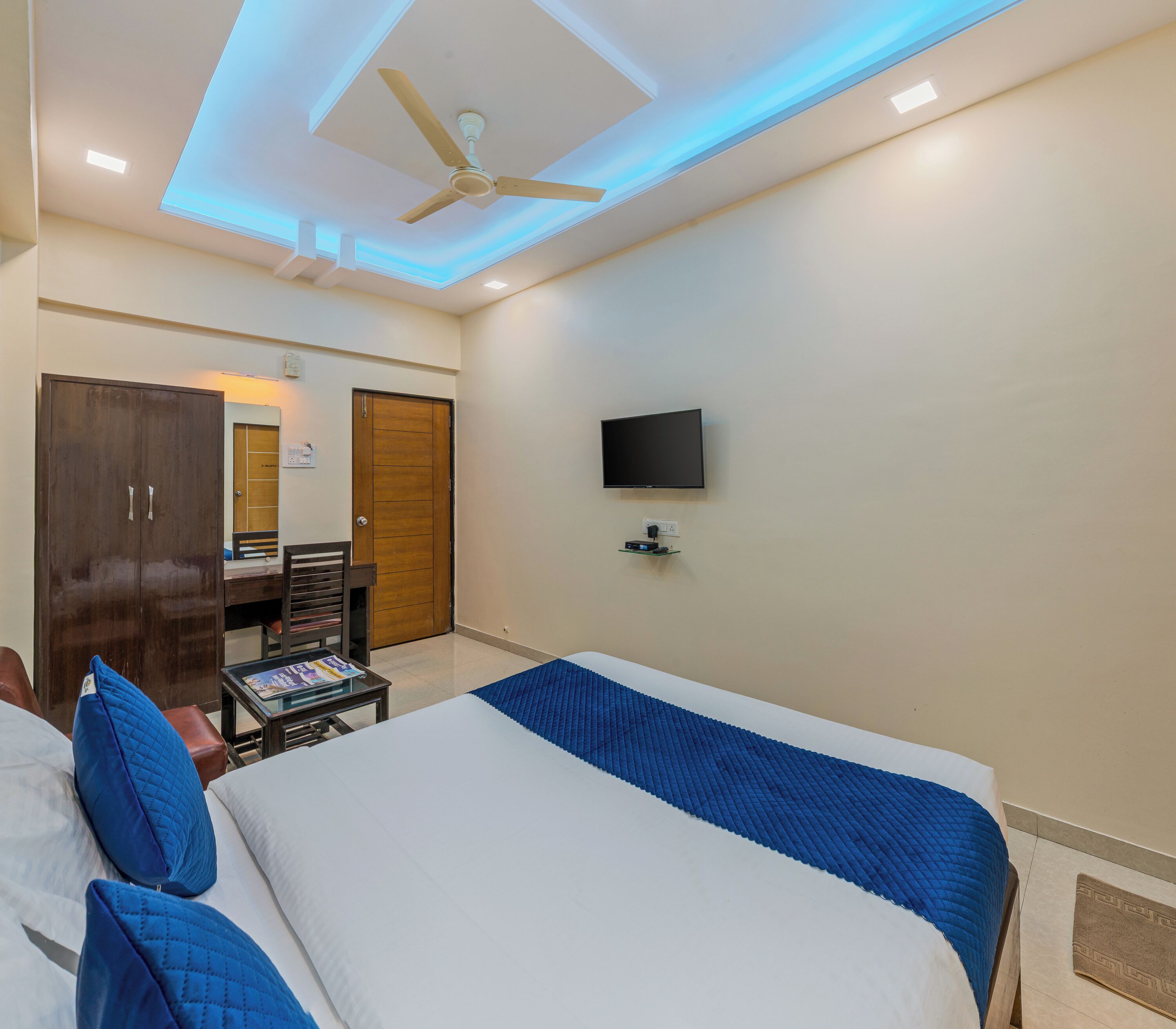 Habitación de hotel con cama, escritorio, silla, armario y televisor montado en la pared.