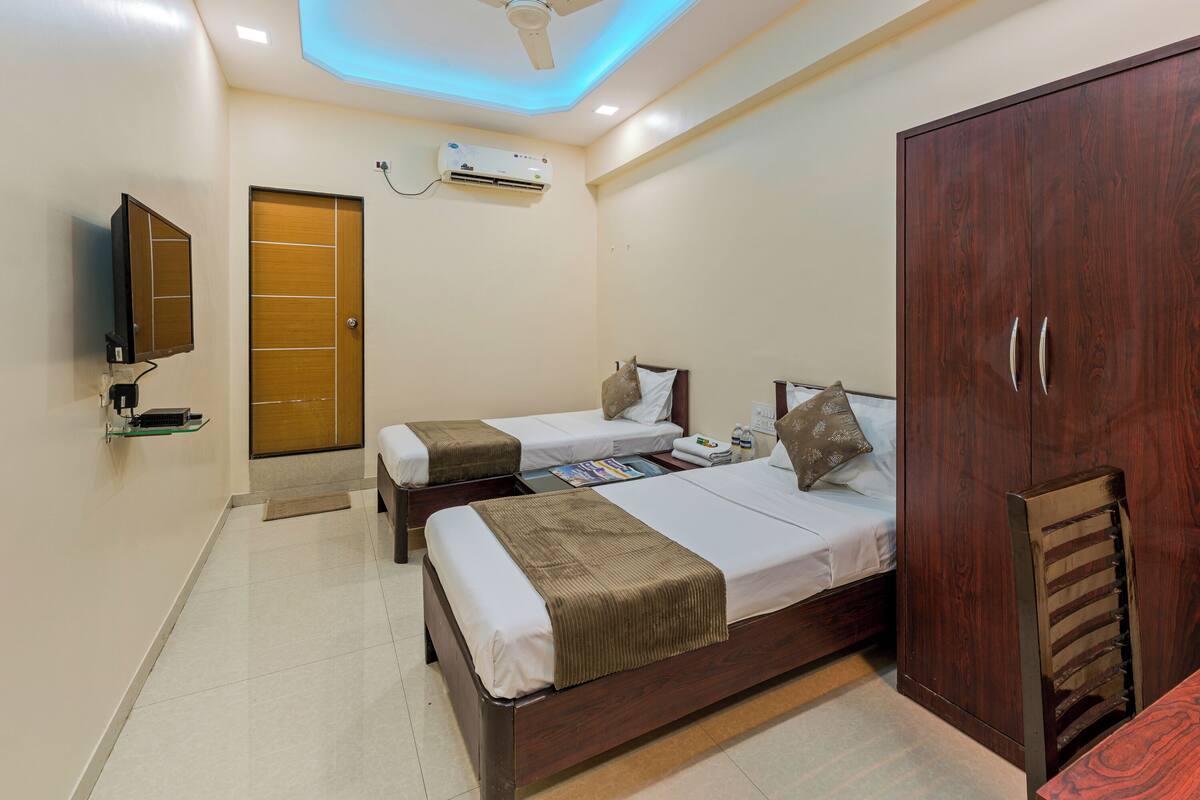 A hotel room with two beds, a wardrobe, a television, and an air conditioning unit.