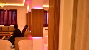 A hotel lobby with a modern design, featuring a seating area with white chairs and a sofa, a chandelier, and wooden paneling on the walls. - Sagar Luminoire Hotel (Patna)