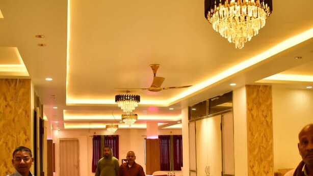 A hotel corridor with a chandelier, marble walls, and a blue tablecloth-covered area in the distance. - Sagar Luminoire Hotel (Patna)