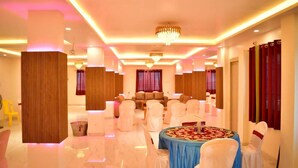 A spacious banquet hall with round tables, white chairs, and a chandelier. - Sagar Luminoire Hotel (Patna)