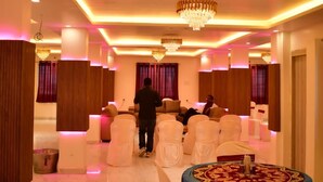 A spacious hall with a polished marble floor, white chairs arranged around a central table, and a chandelier. - Sagar Luminoire Hotel (Patna)