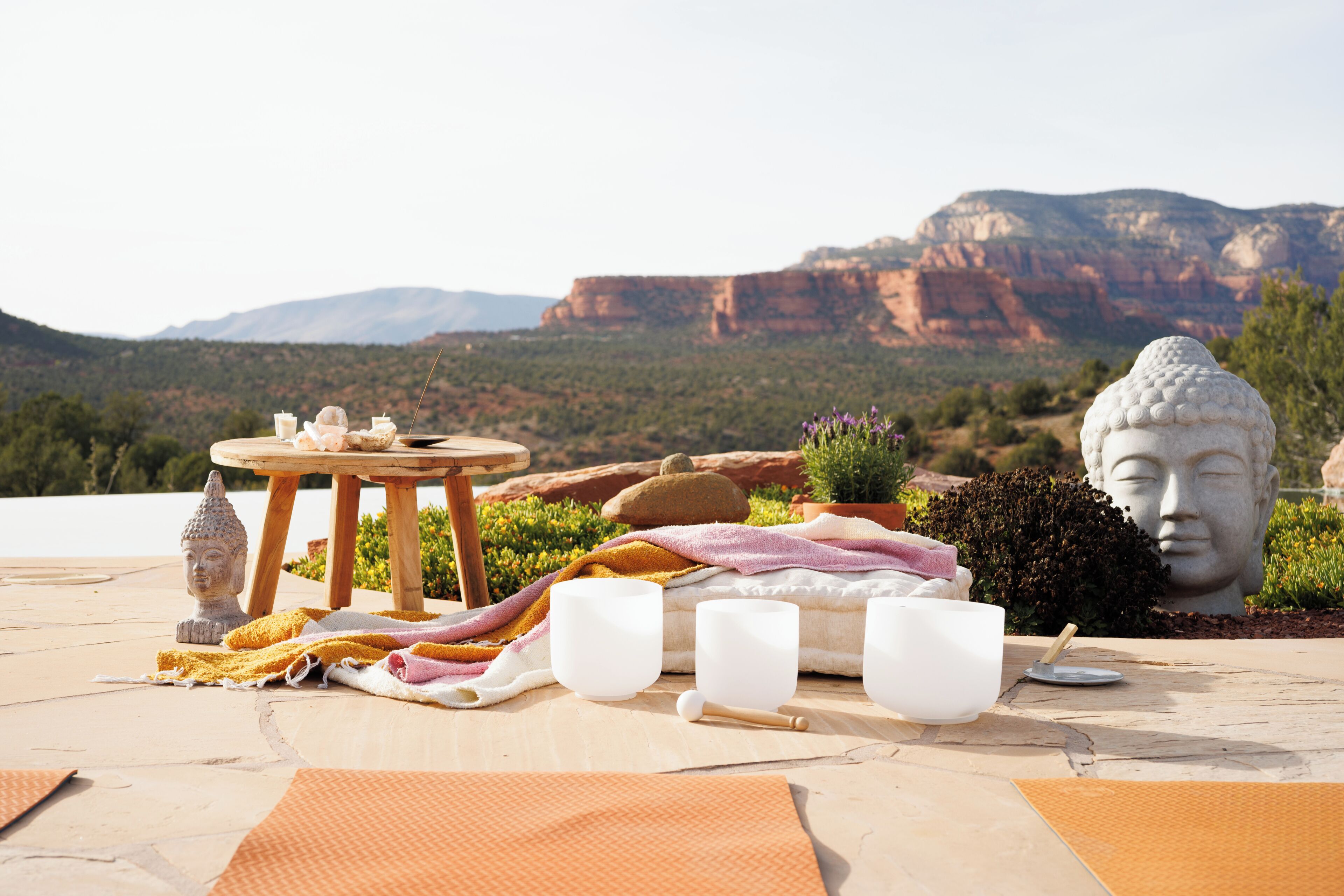 A serene outdoor setting with a table set for a tea ceremony, featuring a Buddha statue, a wooden table, and a scenic mountain backdrop.