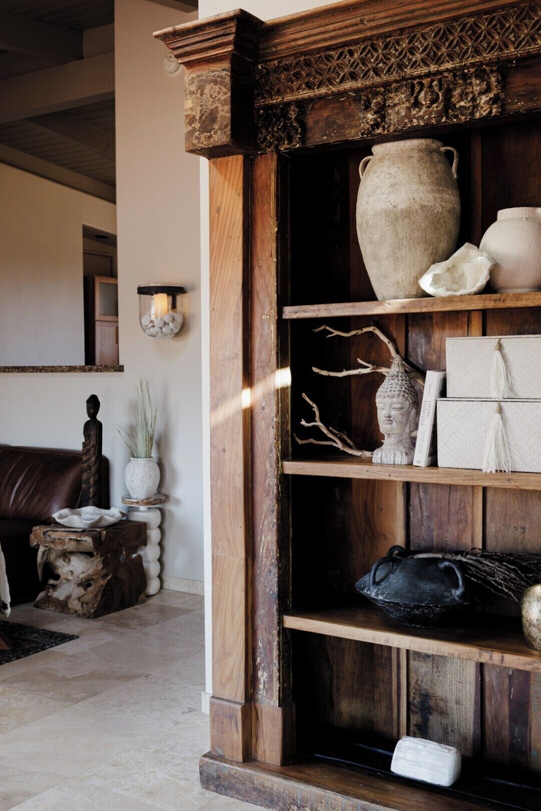 A rustic interior with a wooden shelf displaying pottery and a stone vase.