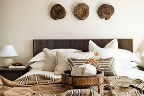 Een net opgemaakt bed met een hoofdbord, een nachtkastje met een lamp, en een decoratief object aan de muur erboven.