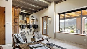 A spacious living area with a large wooden table, several chairs, and a view of a mountainous landscape through large windows. - Sedona Infinity Pool Paradise | Red Rock Views | Hot Tub (Sedona)