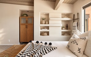 A bedroom with a bed, a wooden wardrobe, built-in shelves, and a window with curtains.