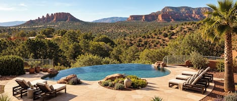 A pool with a view of red rock formations, surrounded by lounge chairs and potted plants.