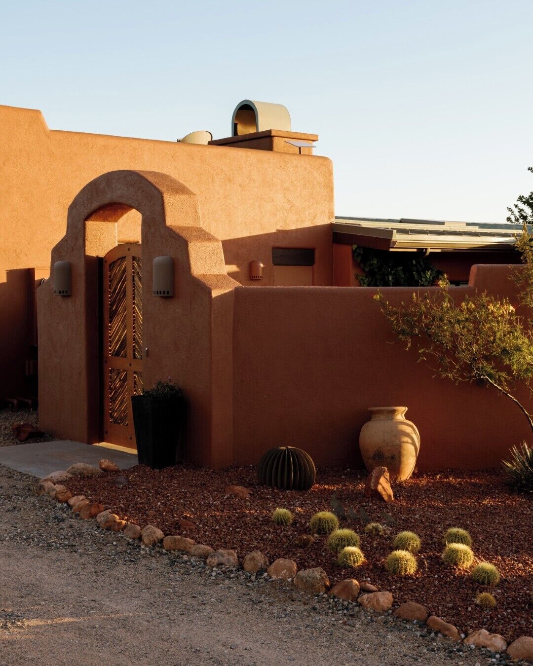 A building with a stucco exterior, a large arched entrance, and a small garden with cacti and rocks.