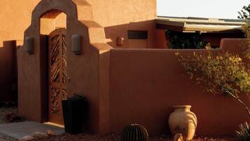 A building with a stucco exterior, a large arched entrance, and a small garden with cacti and rocks.