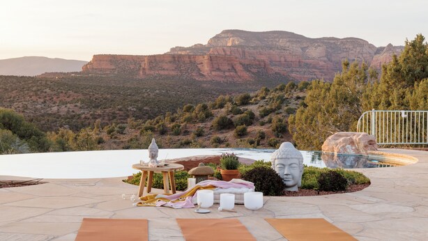 A patio with a Buddha statue, a small table with a Buddha statue, a potted plant, and a stone sculpture. - Sedona Infinity Pool Paradise | Red Rock Views | Hot Tub (Sedona)