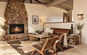 A cozy living room with a stone fireplace, leather sofa, wooden chairs, and a coffee table.