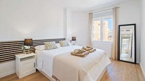 A modern bedroom with a large bed, bedside tables, a mirror, and a window with curtains.
