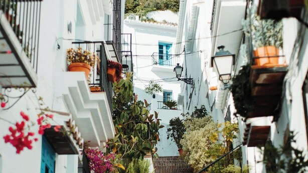 A narrow street with white buildings, red brick steps, and potted plants.