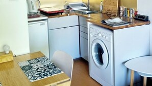 A compact kitchen with white cabinets, a washing machine, a microwave, and a small dining area with a table and chairs.