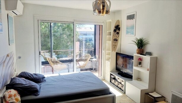 A bedroom with a bed, a TV, a surfboard, and a balcony with chairs.