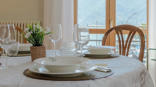 A dining table set with plates, glasses, and a centerpiece, overlooking a mountainous landscape through large windows. - Casa MAMMA, family relaxation on Lake Iseo - elegant apartment - 2 rooms (Lovere)