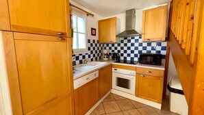 A compact kitchen with wooden cabinets, a checkered backsplash, a microwave, a stove, and a dishwasher. - Charming villa 6 pers, quiet residence, private pool (Saint-Jean-de-Monts)