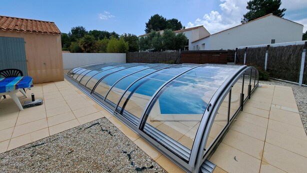 A covered outdoor area with a table and chairs, a small shed, and a white building in the background. - Charming villa 6 pers, quiet residence, private pool (Saint-Jean-de-Monts)
