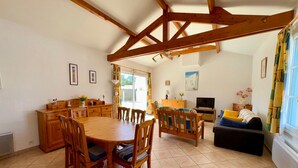 A spacious living area with a wooden dining table, chairs, a sofa, and a TV. - Charming villa 6 pers, quiet residence, private pool (Saint-Jean-de-Monts)
