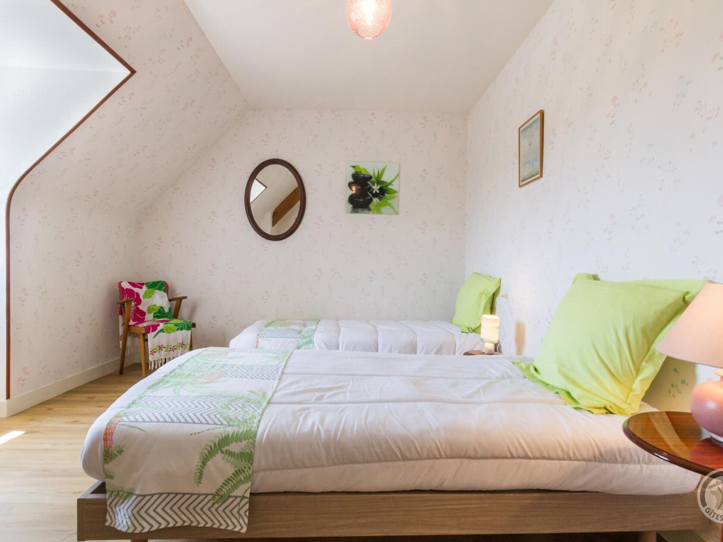 Un dormitorio con una cama, una silla, un espejo, una planta en la pared y una lámpara.