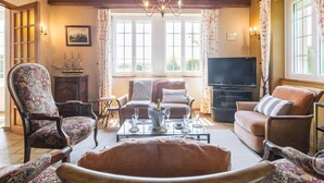 Ein gemütliches Wohnzimmer mit Holzbalken, einem Chandelier, einem Fernseher und einem großen Fenster mit Vorhängen.
