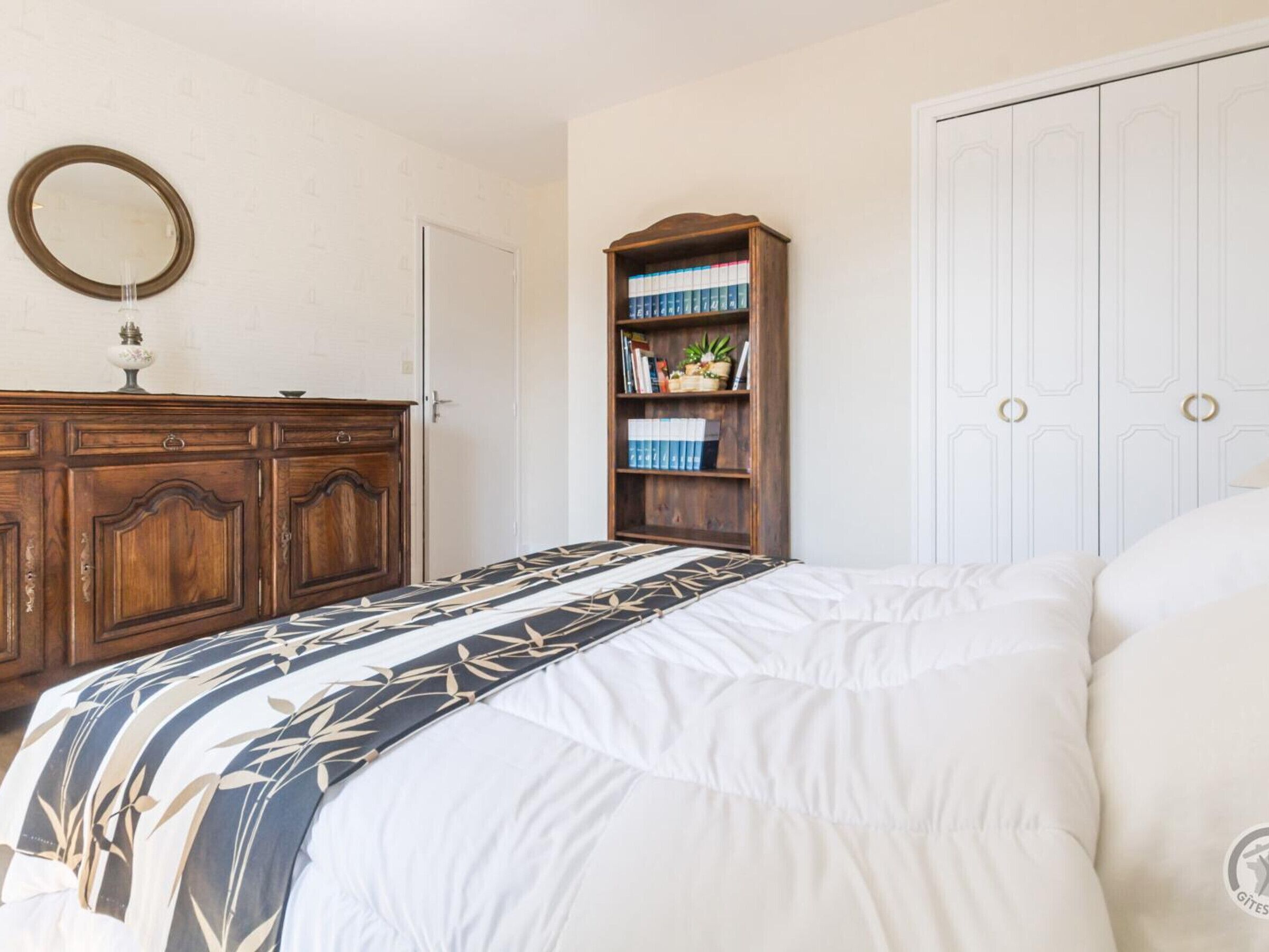 A bedroom with a bed, a wooden dresser, a bookshelf, and a white wardrobe.