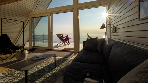 A cozy interior with a large window overlooking a beach, a comfortable couch, and a chair.