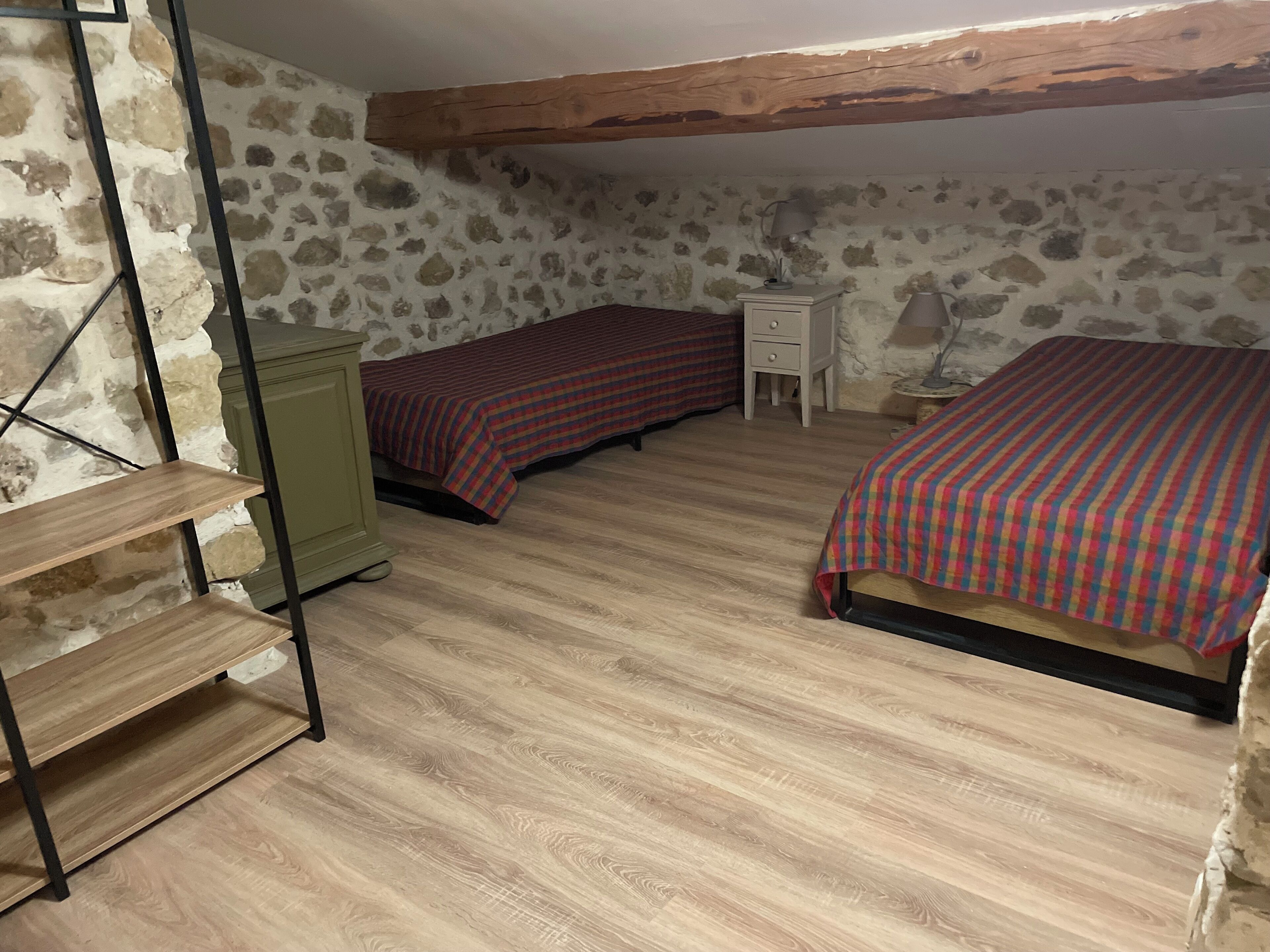 Una camera da letto con due letti, pavimento in legno, parete in pietra e trave in legno al soffitto.