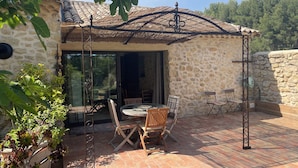 A stone building with a tiled roof, a glass door leading inside, and a patio area with a table and chairs. - Gite in superb stone farmhouse in idyllic setting, 10 minutes from beaches. (Le Castellet)