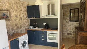A compact kitchen with a washing machine, a coffee maker, and a stove. - Gite in superb stone farmhouse in idyllic setting, 10 minutes from beaches. (Le Castellet)