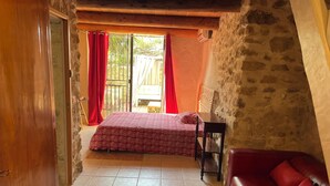 A bedroom with a bed, a wooden chair, a red sofa, and a stone wall. - Gite in superb stone farmhouse in idyllic setting, 10 minutes from beaches. (Le Castellet)